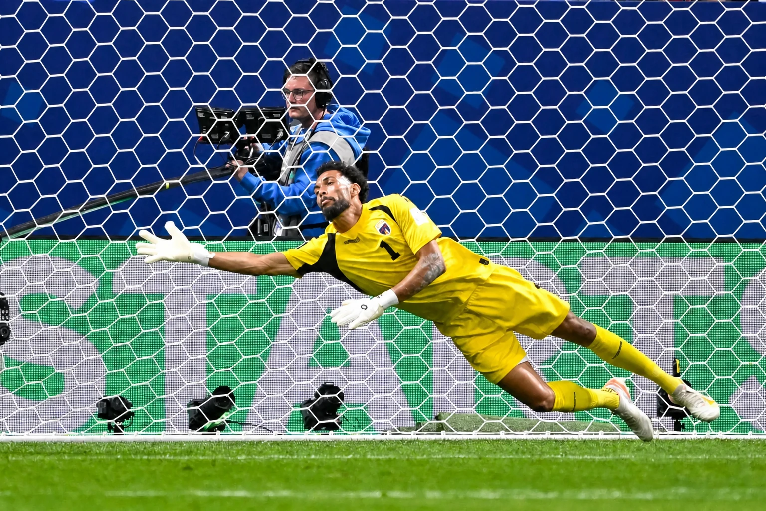 A goalkeeper in yellow dives toward an off-screen ball to the viewer's left.